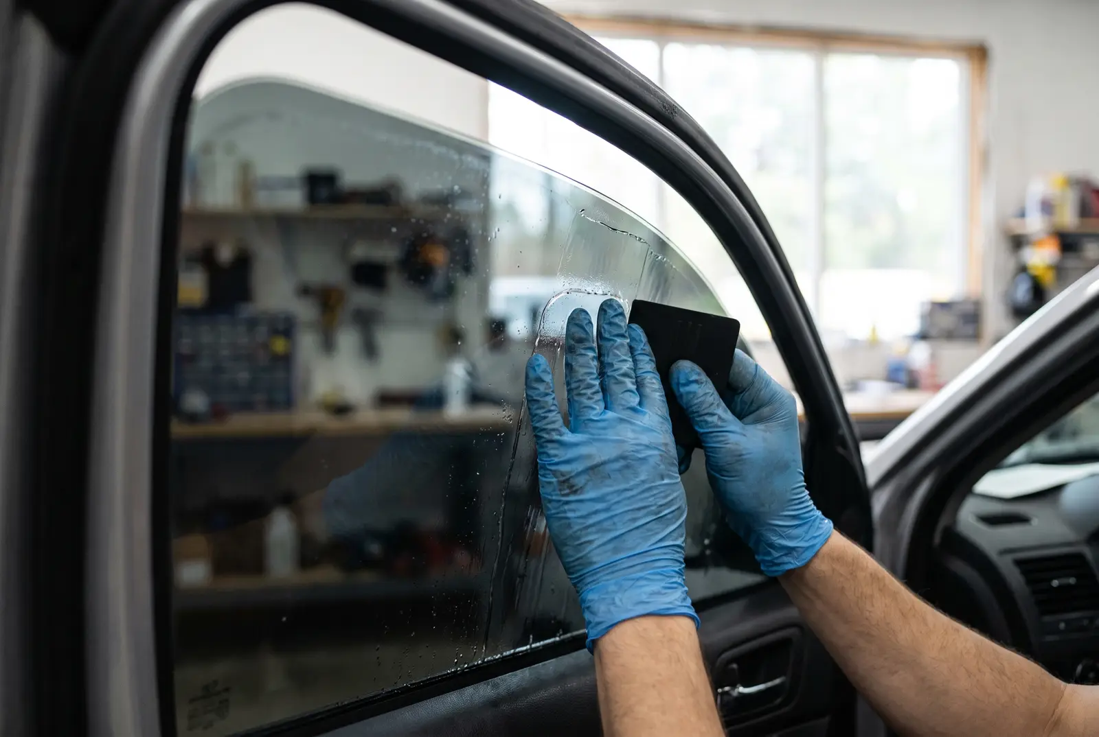 An installer squeegeeing ceramic window tint onto a car door glass from inside the vehicle